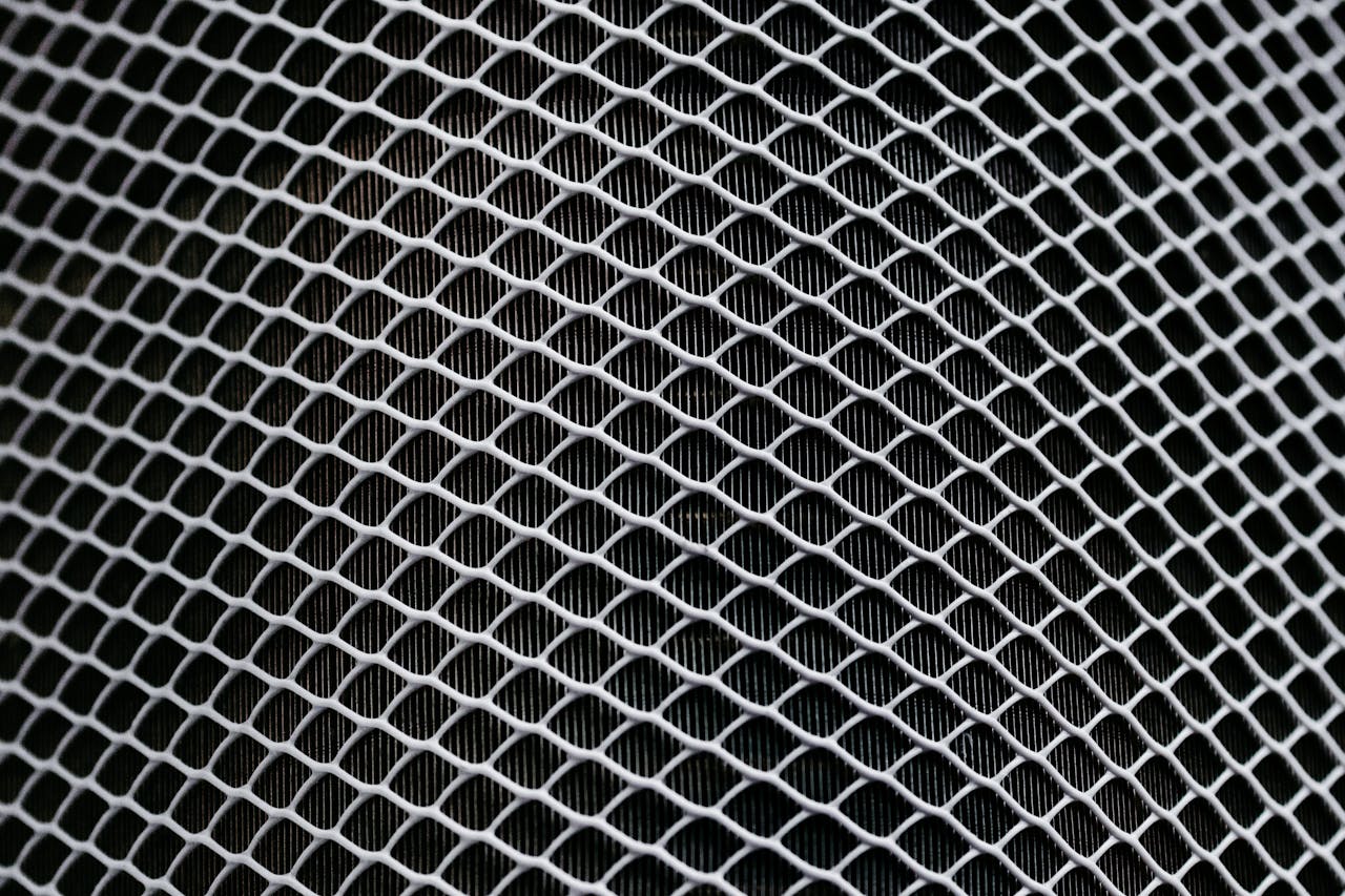 Detailed texture of industrial metal mesh with geometric patterns and shadows.