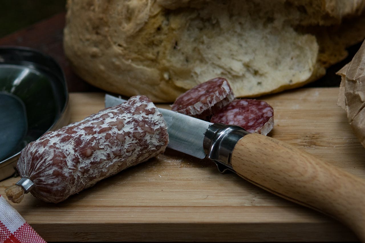 A rustic scene of fresh bread and salami on a wooden board with a knife, perfect for culinary presentations.